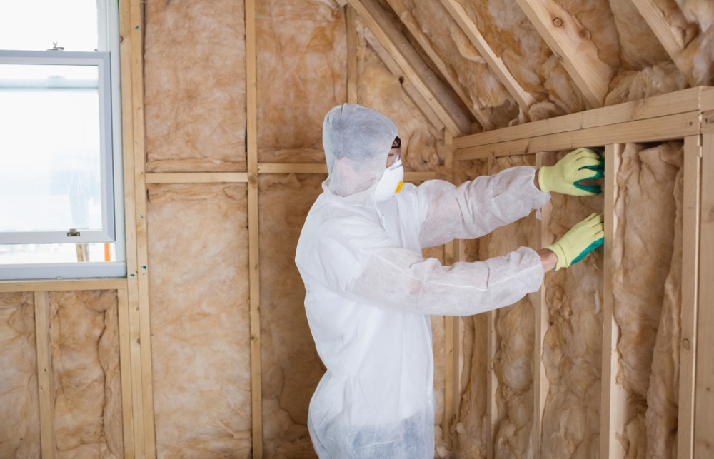 Installer fitting fiberglass batts between wall studs