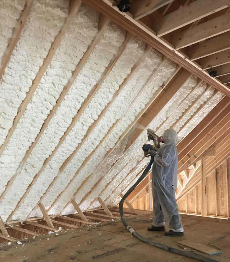 Installer spraying foam insulation along an attic roofline